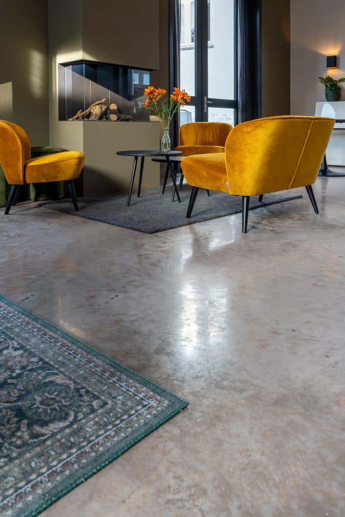 Detailfoto van een woonbetonvloer in de kleur 'June Sand' (donkerbruine betonvloer), met open haard en zithoek